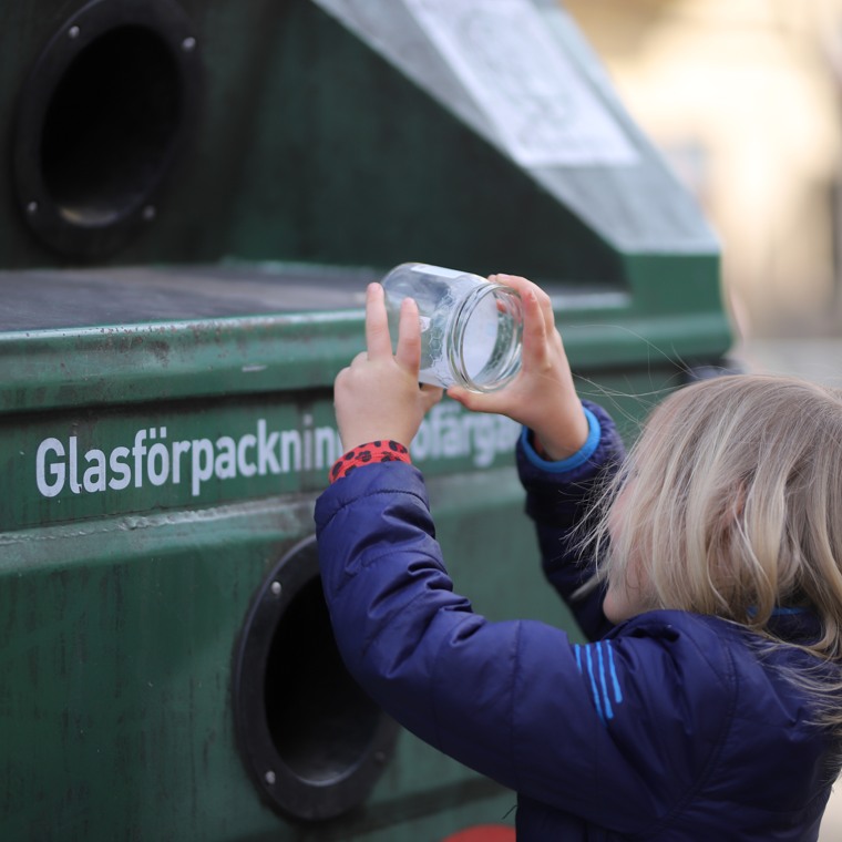 Barn som lägger en glasburk i återvinningsbehållare för glasförpackningar på en återvinningsstation.